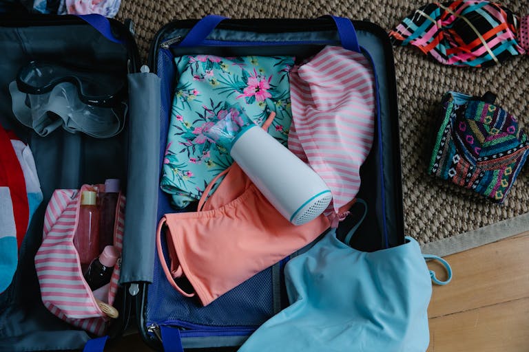 A packed suitcase with swimwear, goggles, and essentials for a summer trip.